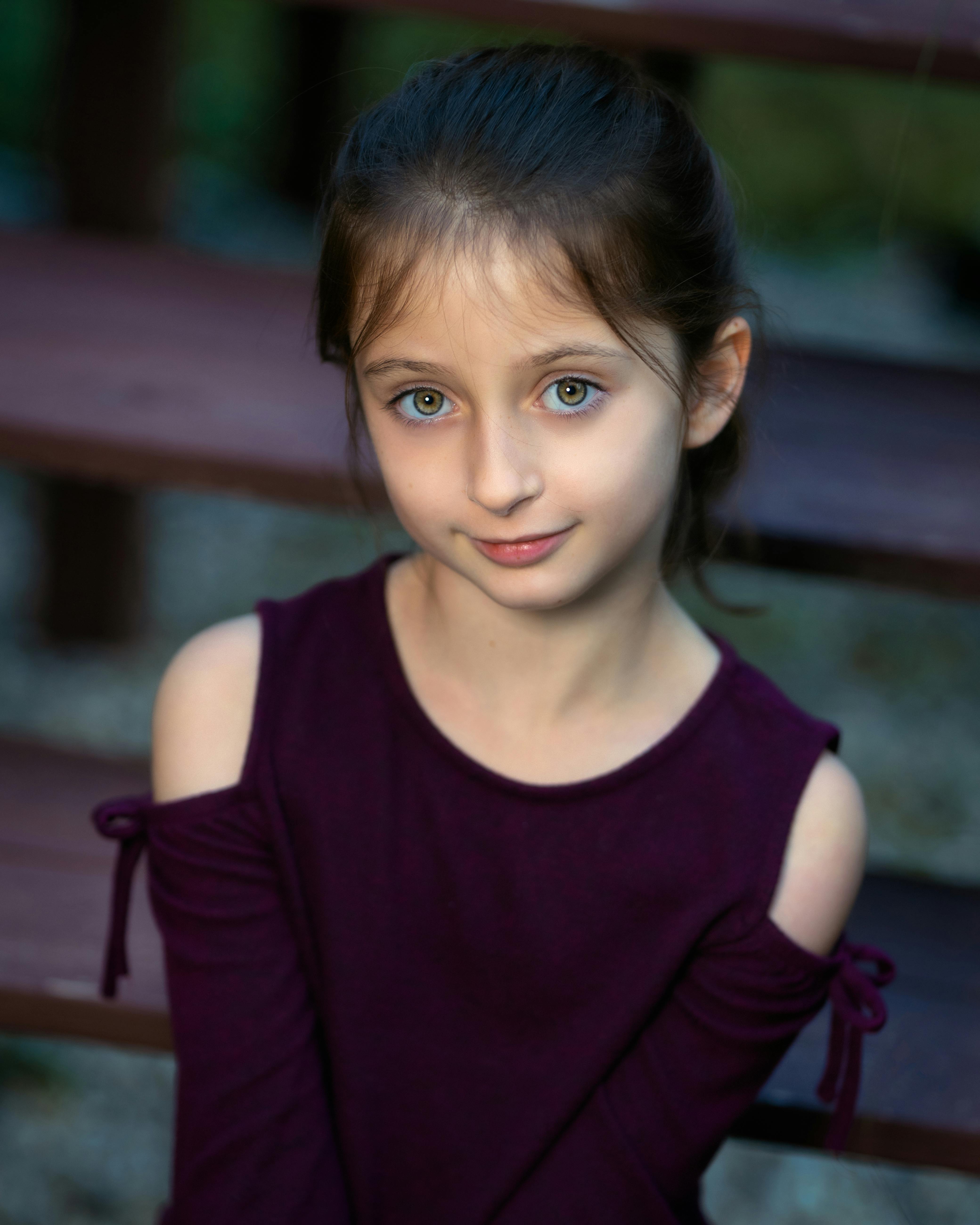 Little cheerful stylish girl smiling and looking at camera on blurred background of yard