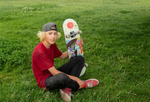 Boy Sitting on Grass Holding a Skateboard