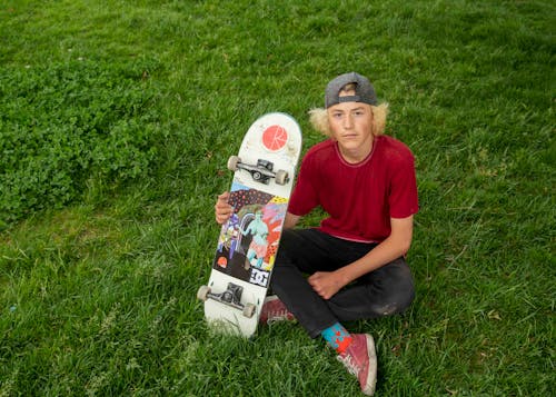 Boy Sitting on Grass Posing with a Skateboard