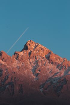 Capture of the stunning Demirkazık mountain with a clear blue sky and contrail at sunset.