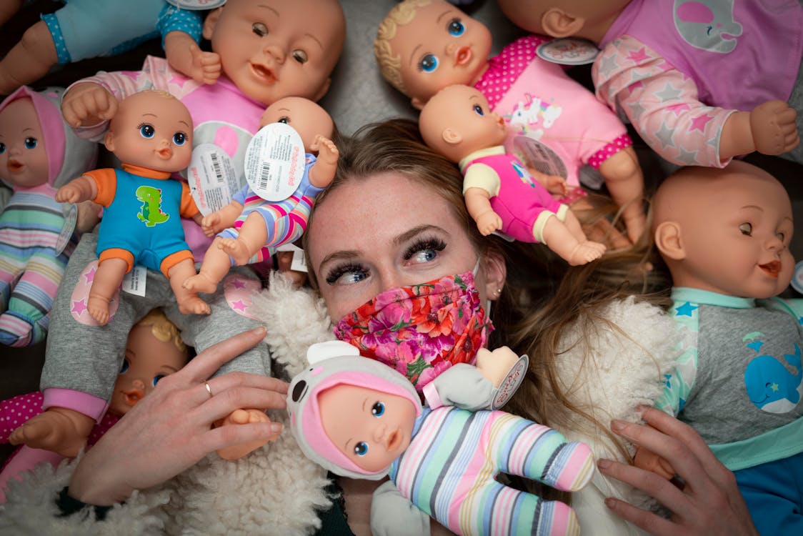 Free Woman Wearing Face Mask Surrounded by Dolls Stock Photo