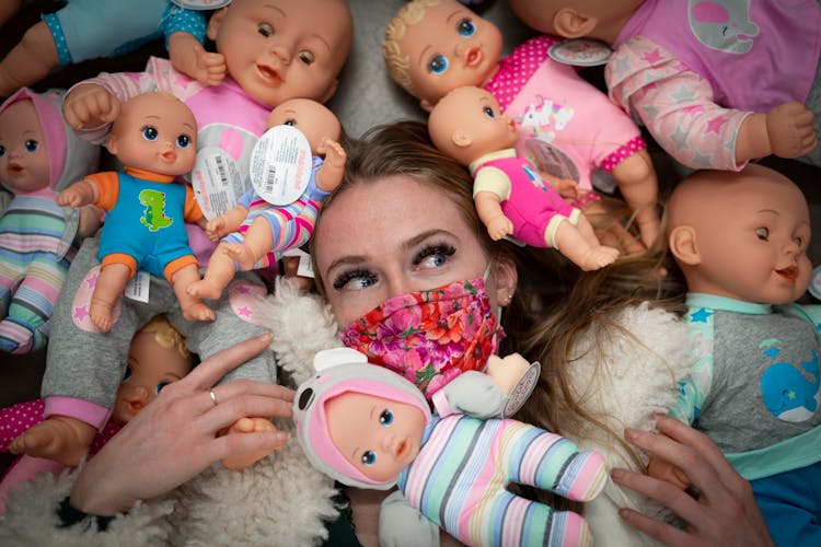 Woman Wearing Face Mask Surrounded By Dolls