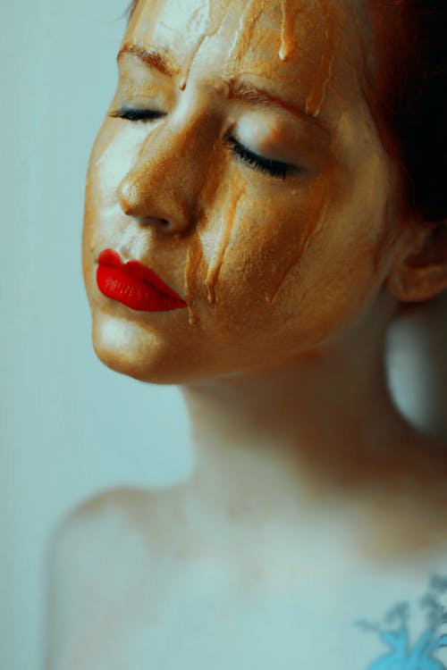 A Woman With Red Lipstick and Gold Melting Paint on Her Face