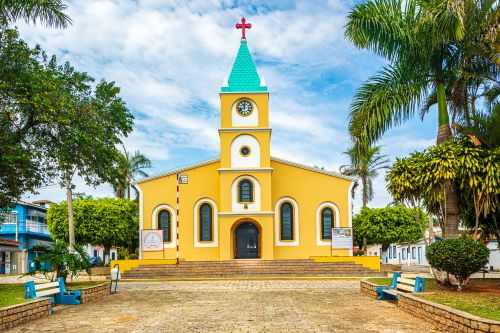 Free Bright yellow church with palm trees in Alambari, Brazil under a clear blue sky. Stock Photo