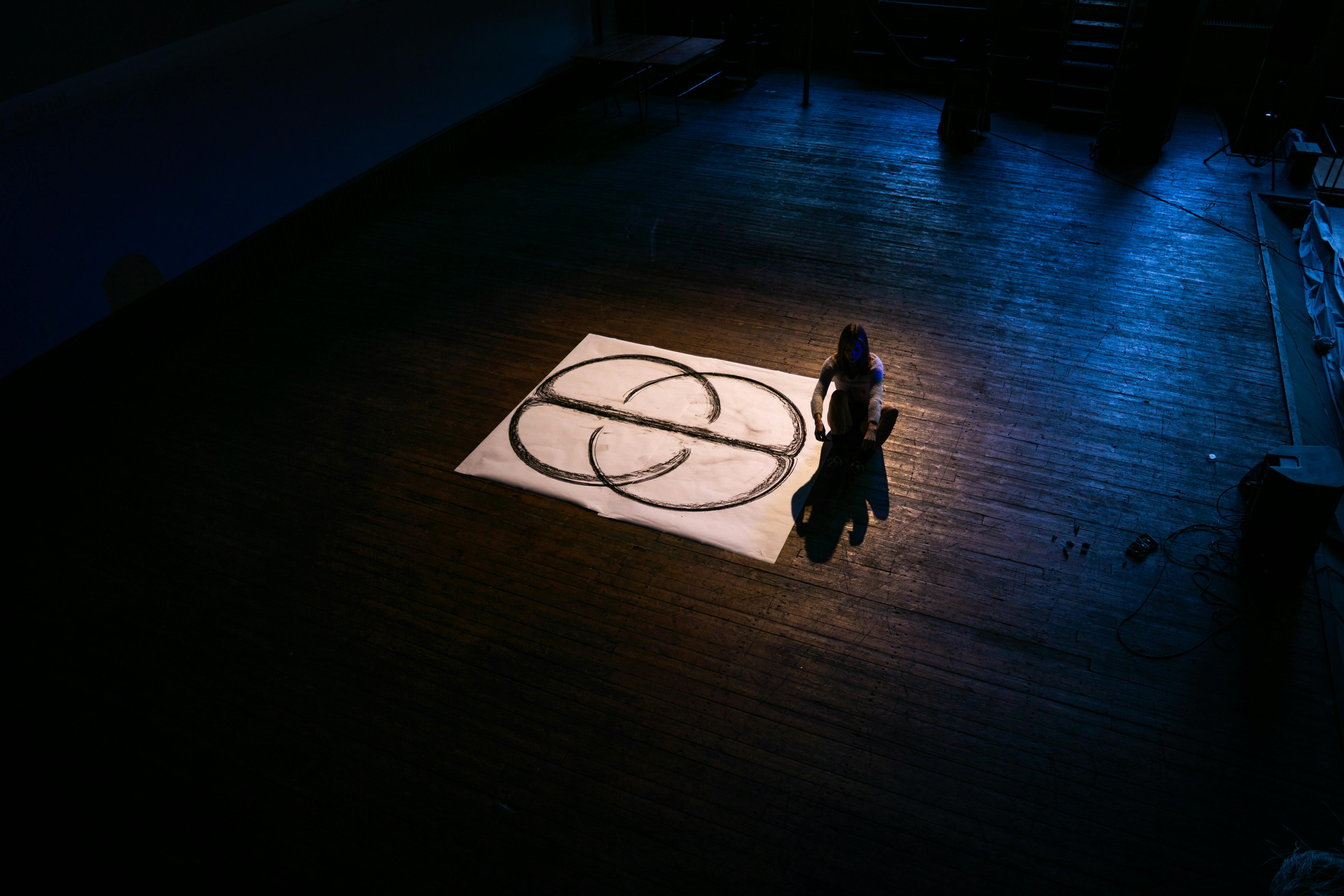 Free A lone performer onstage interacts with a geometric design illuminated by spotlight. Stock Photo