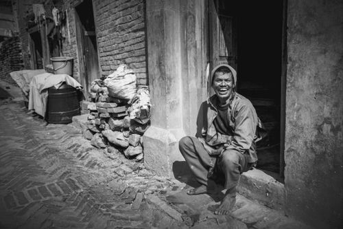 Free A candid black and white portrait of a man sitting barefoot by a brick wall in Kathmandu, Nepal. Stock Photo