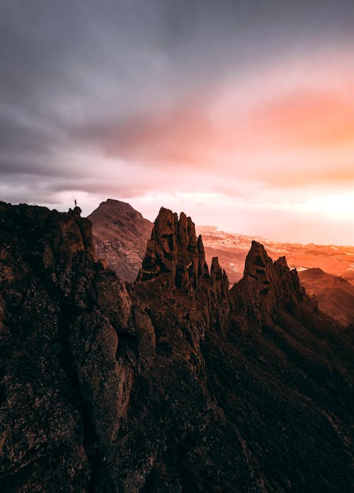 Picturesque scenery of top of rocky mountains placed in countryside under cloudy colorful sky at sunrise