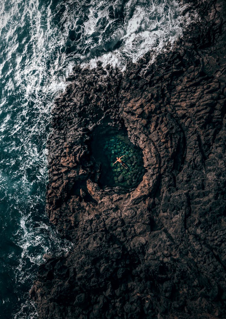 Person Swimming In Pool In Rock Near Wavy Ocean In Daytime