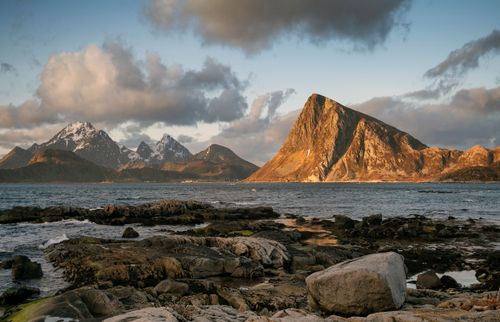 Free A stunning view of snowcapped mountains and a rocky coast under a dramatic cloudy sky. Stock Photo