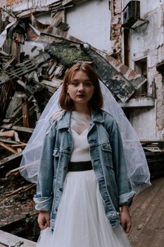 A bride in a denim jacket stands amidst urban ruins, blending fashion and decay.