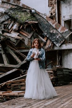 A young woman in a wedding dress stands stylishly in an abandoned building.