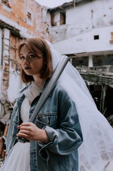 Bride in denim jacket with bat in abandoned building setting.