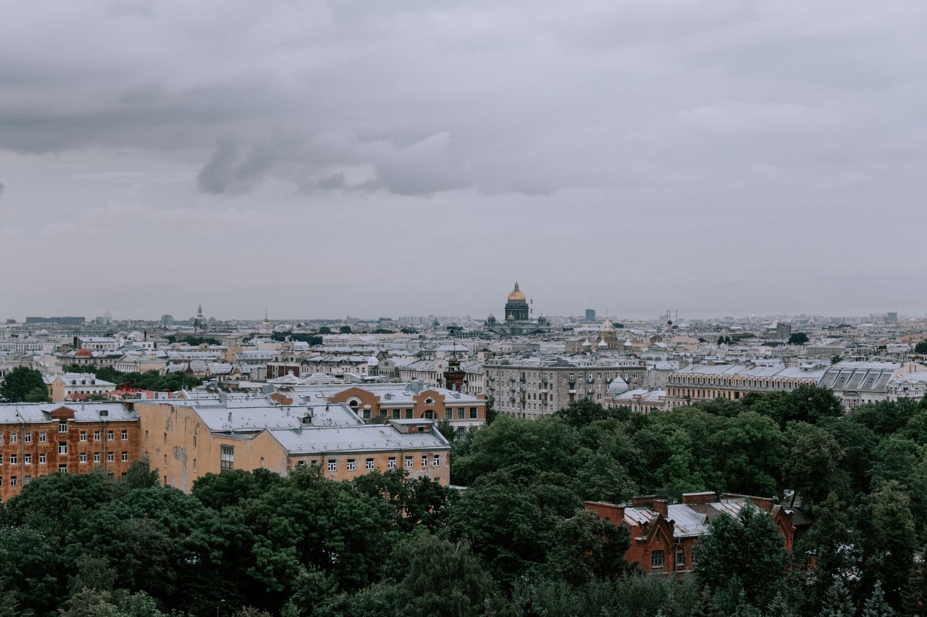 A panoramic view capturing a city's skyline with lush greenery and overcast skies.