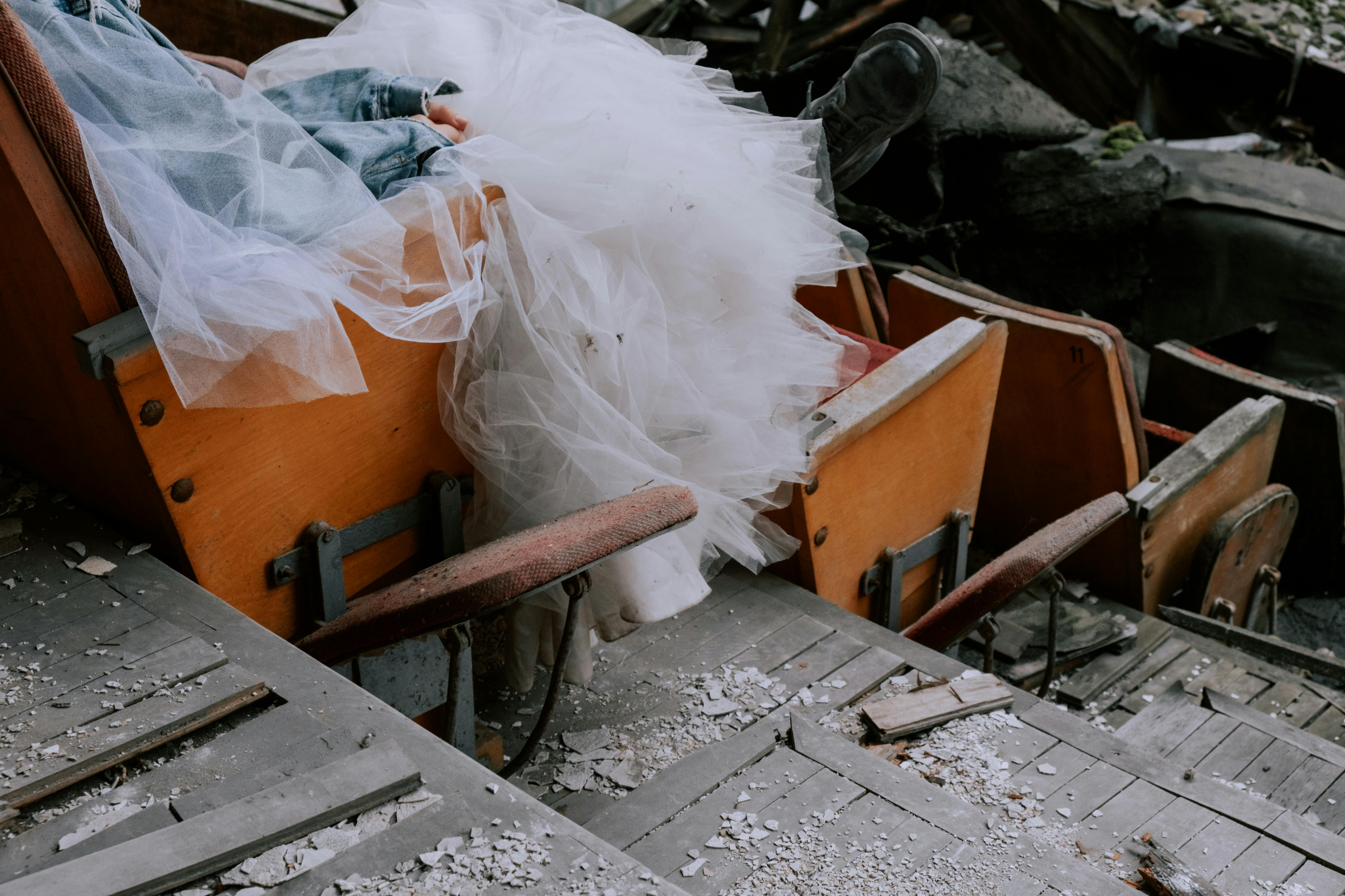 Free A bride in a denim jacket sits in an abandoned theater, surrounded by wooden chairs. Stock Photo