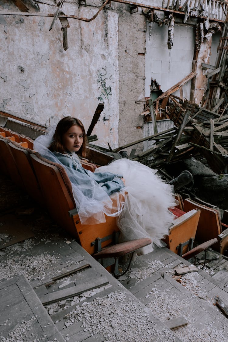 A Young Woman Wearing A Wedding Dress Sitting On Theater Chair In A Ruined Building