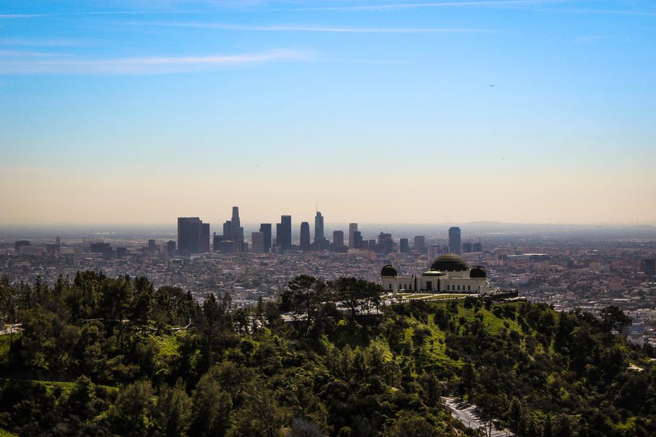 Panoramic view of Los Angeles cityscape with Griffith Observatory in the foreground under a clear sky.