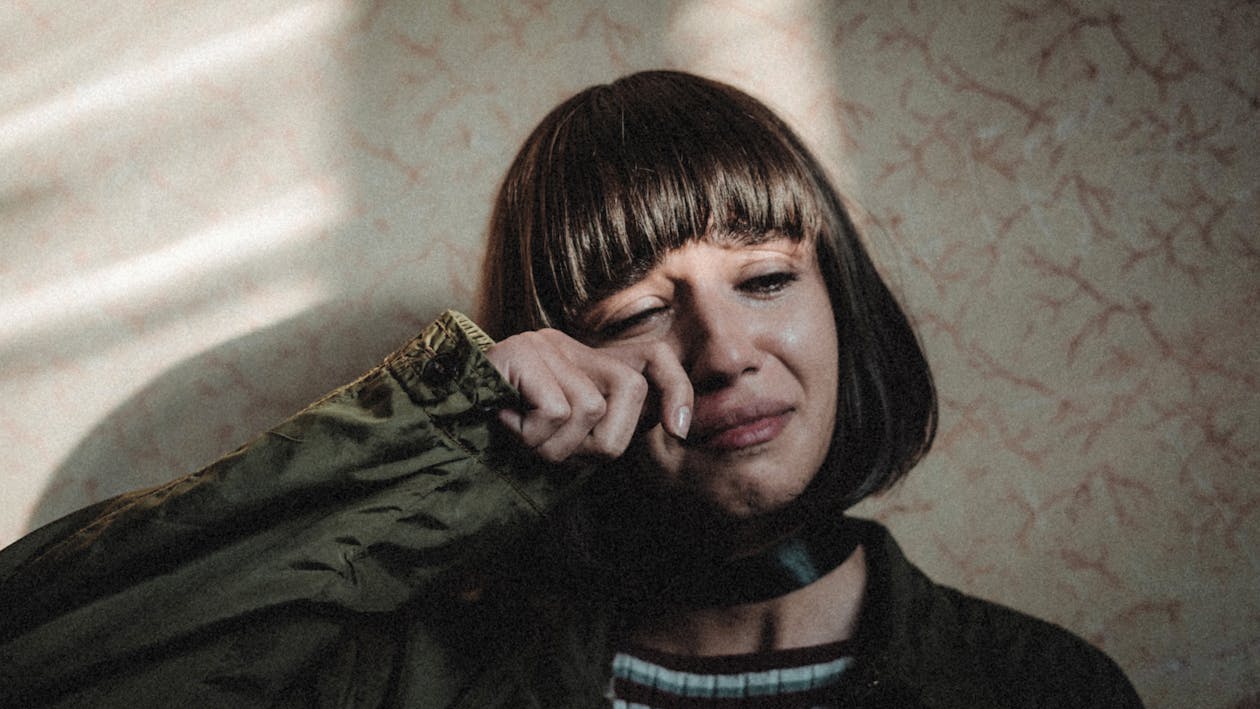 Unhappy female with modern haircut wiping tears while leaning on wall in room Friendsgiving