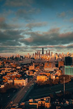 A captivating aerial view of a city skyline at sunrise with dramatic clouds and warm sunlight.