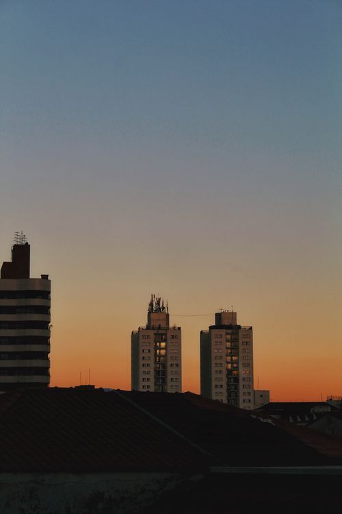Free Silhouetted city buildings at dusk with a vivid orange and blue sunset sky. Stock Photo