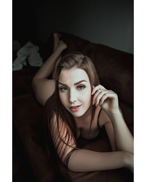 Young smiling female with makeup looking at camera while lying on sofa in house room