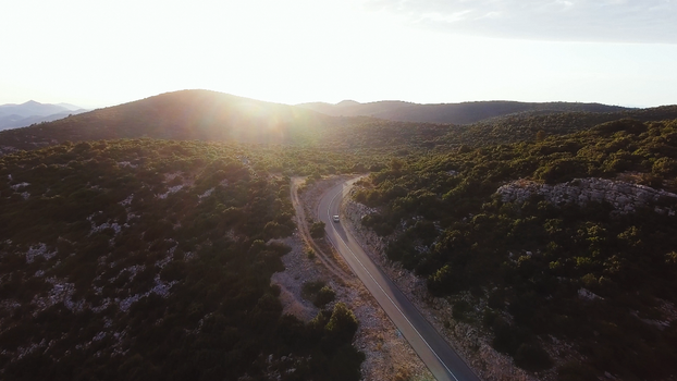 Captivating aerial shot of a winding road through lush hills during a serene sunset.
