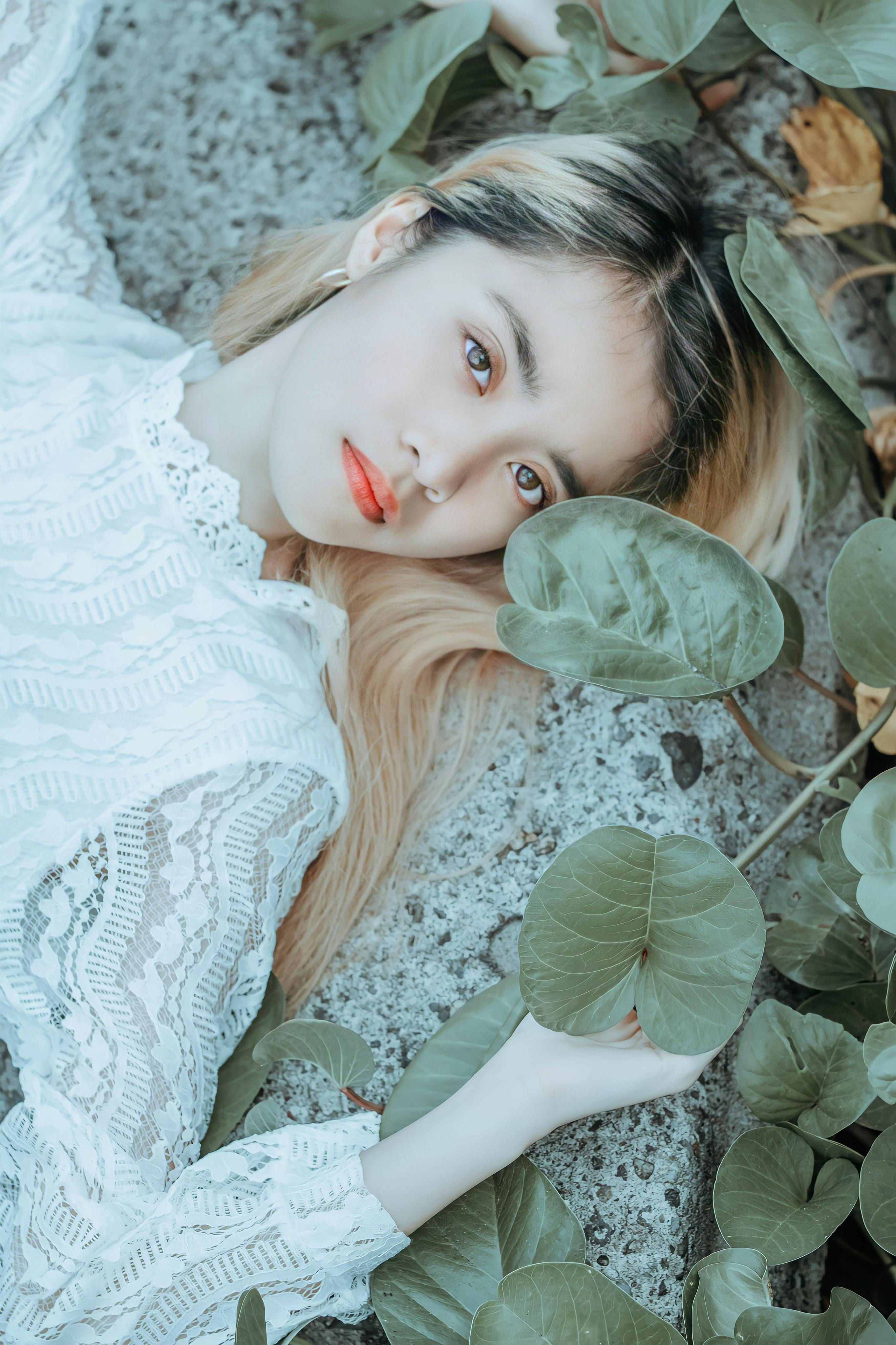 emotionless young woman lying on stone surface and holding plant branch