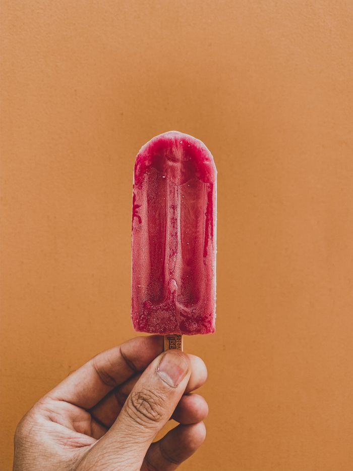 A hand holding a vibrant raspberry ice pop