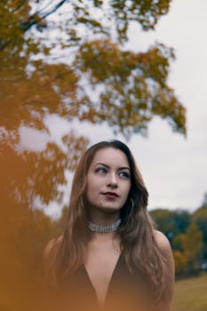 一位美丽的女人在秋叶公园里穿着时尚的服装摆姿势