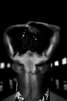 Black and white portrait of a topless man with braids showing muscular back.