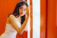 Young Woman in White Dress Leaning on Orange Wall