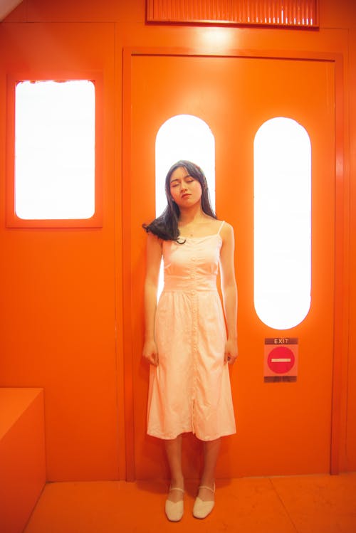 Woman in White Dress Standing Near Orange Door
