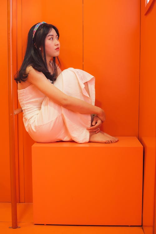 Young Woman in White Dress Sitting on Orange Seat