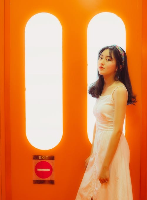 Woman in White Dress Standing Near White Windows in Orange Door