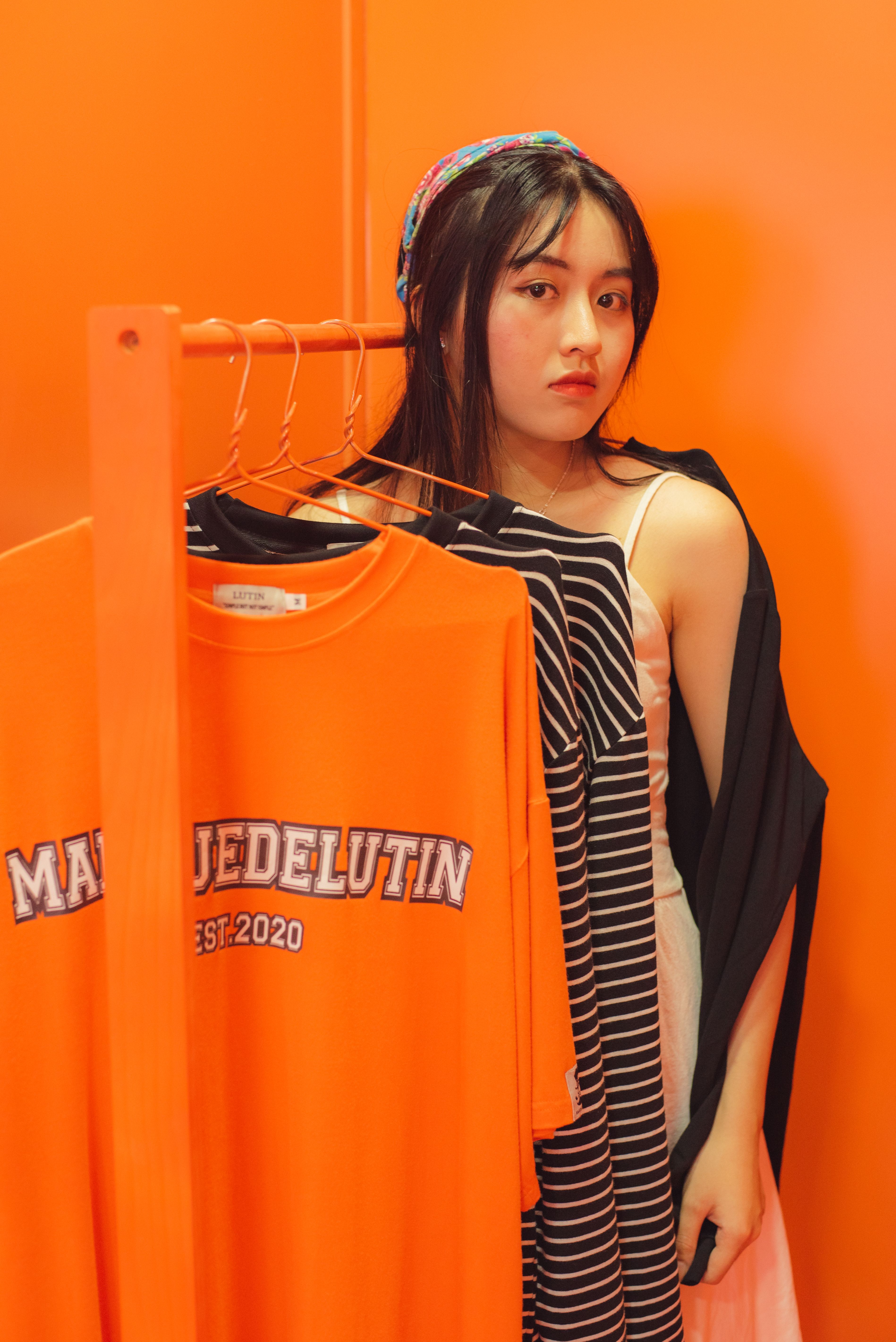 Stylish woman in striped attire standing next to an orange-clad clothes rack against a bold orange background.