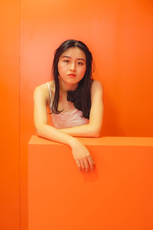 Free Striking portrait of a young woman with black hair posing against a bold orange backdrop. Stock Photo