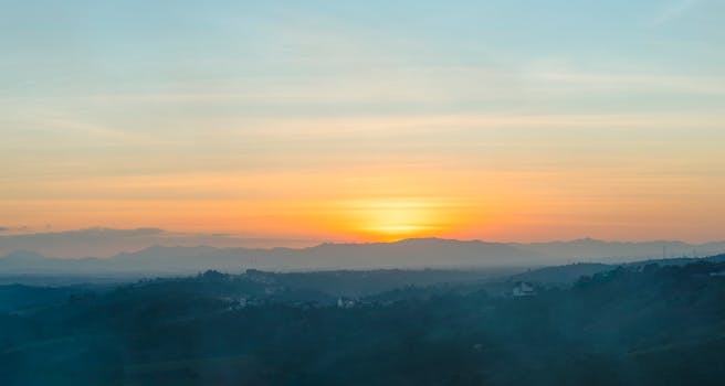 A stunning sunrise view over misty rolling hills with mountains in the background.