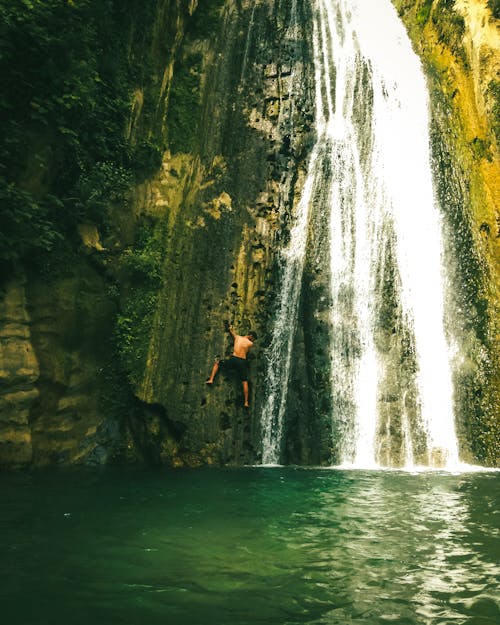 Man Climbing on the Mountain Beside Waterfall