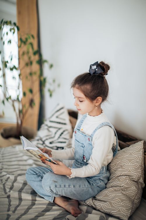Free A young girl attentively reading a book while sitting indoors in a cozy room with soft lighting. Stock Photo