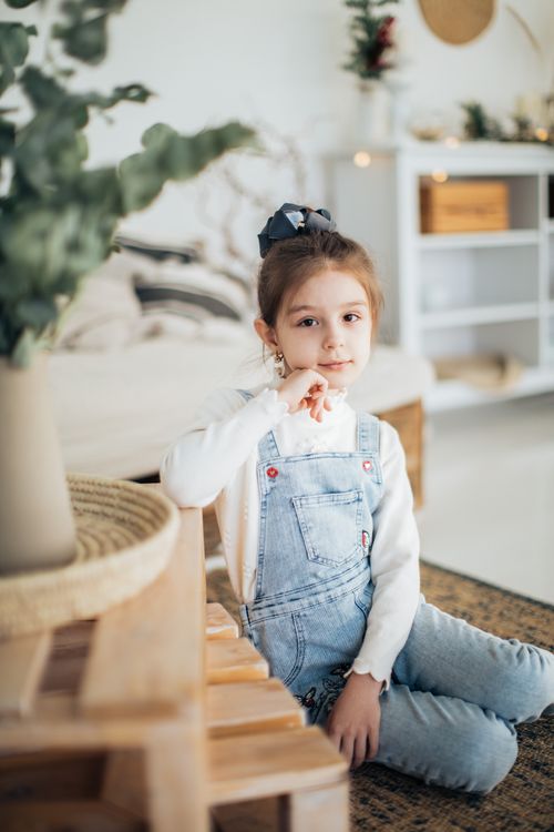 Free A pretty young girl in a cozy indoor setting, wearing casual denim overalls and smiling softly. Stock Photo