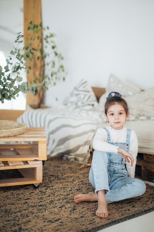 Free A cute young girl sitting on a carpet in a stylish room with natural decor. Stock Photo