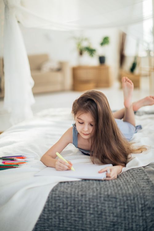 Free A child lying on a bed, focused on drawing with colored pencils, showcasing creativity and concentration. Stock Photo