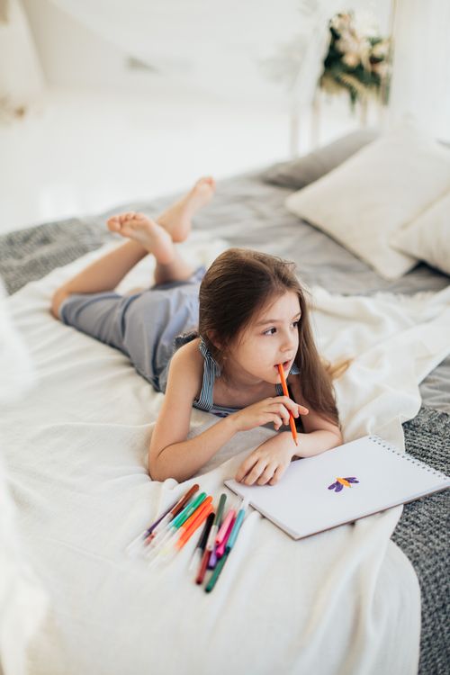 Free Child on bed drawing with colorful markers, showcasing creativity and relaxation indoors. Stock Photo
