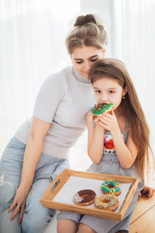 Photo of a Kid Eating a Donut Beside Her Mother