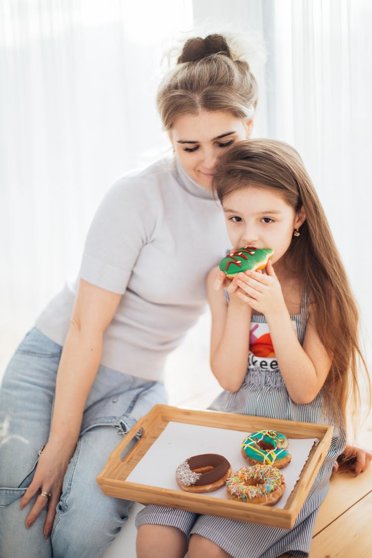 Photo Of A Kid Eating A Donut Beside Her Mother