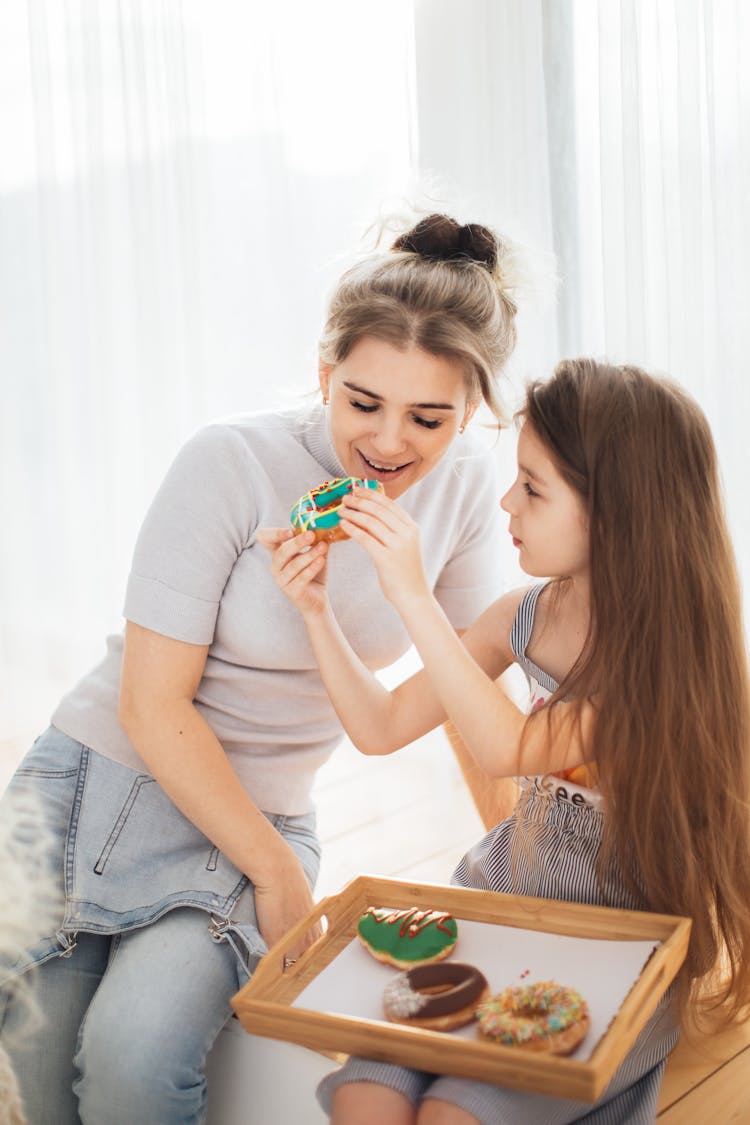 Photograph Of A Kid Feeding A Donut To Her Mother