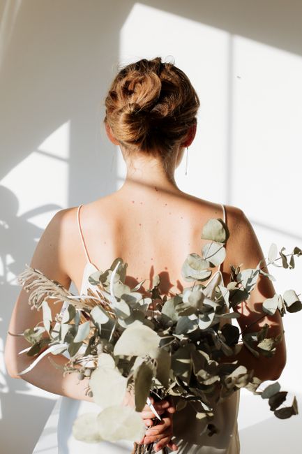 A serene back view of a woman holding eucalyptus branches in sunlight.