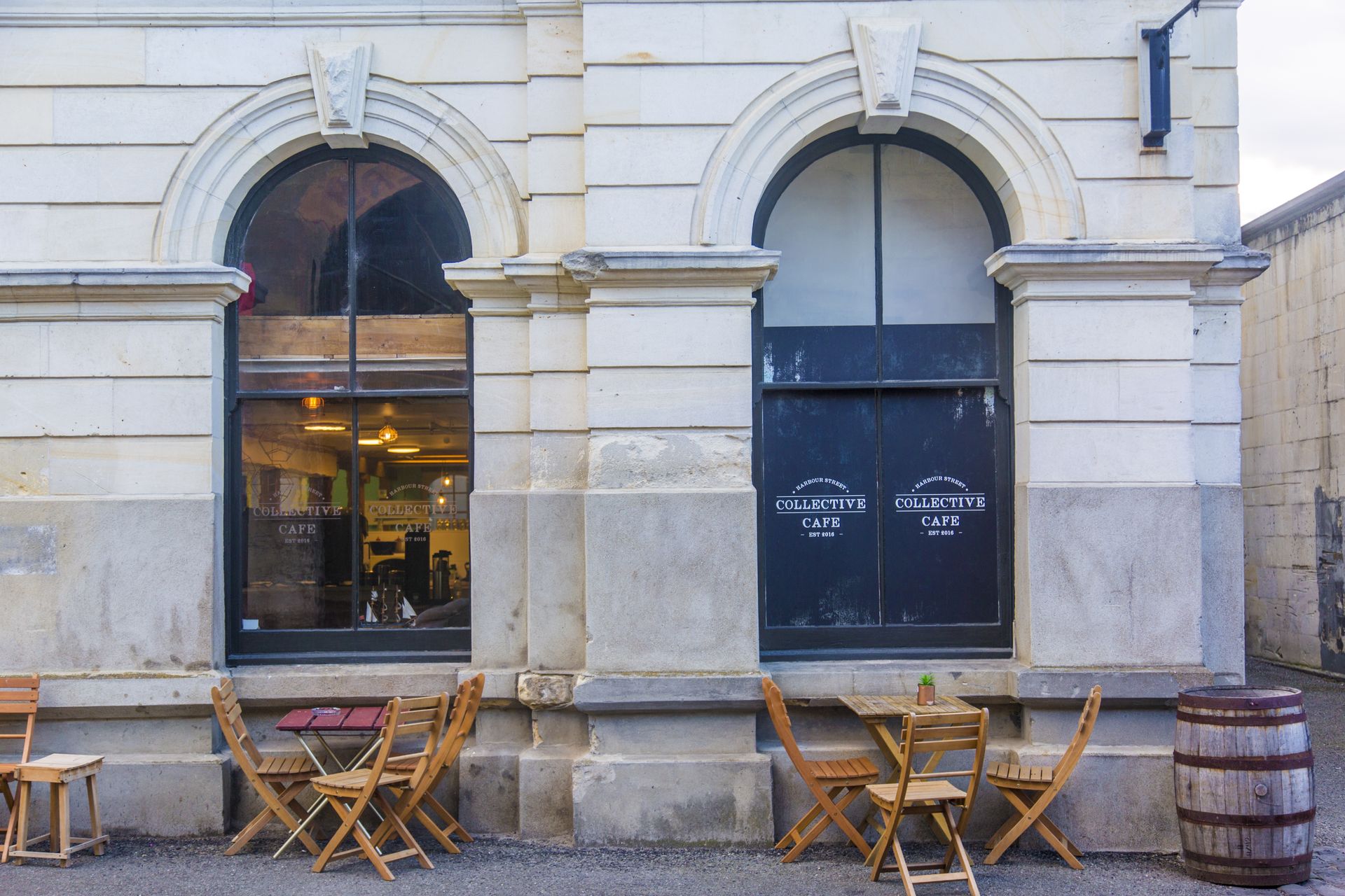 Outdoor café with rustic wooden tables and chairs against a stone building facade.