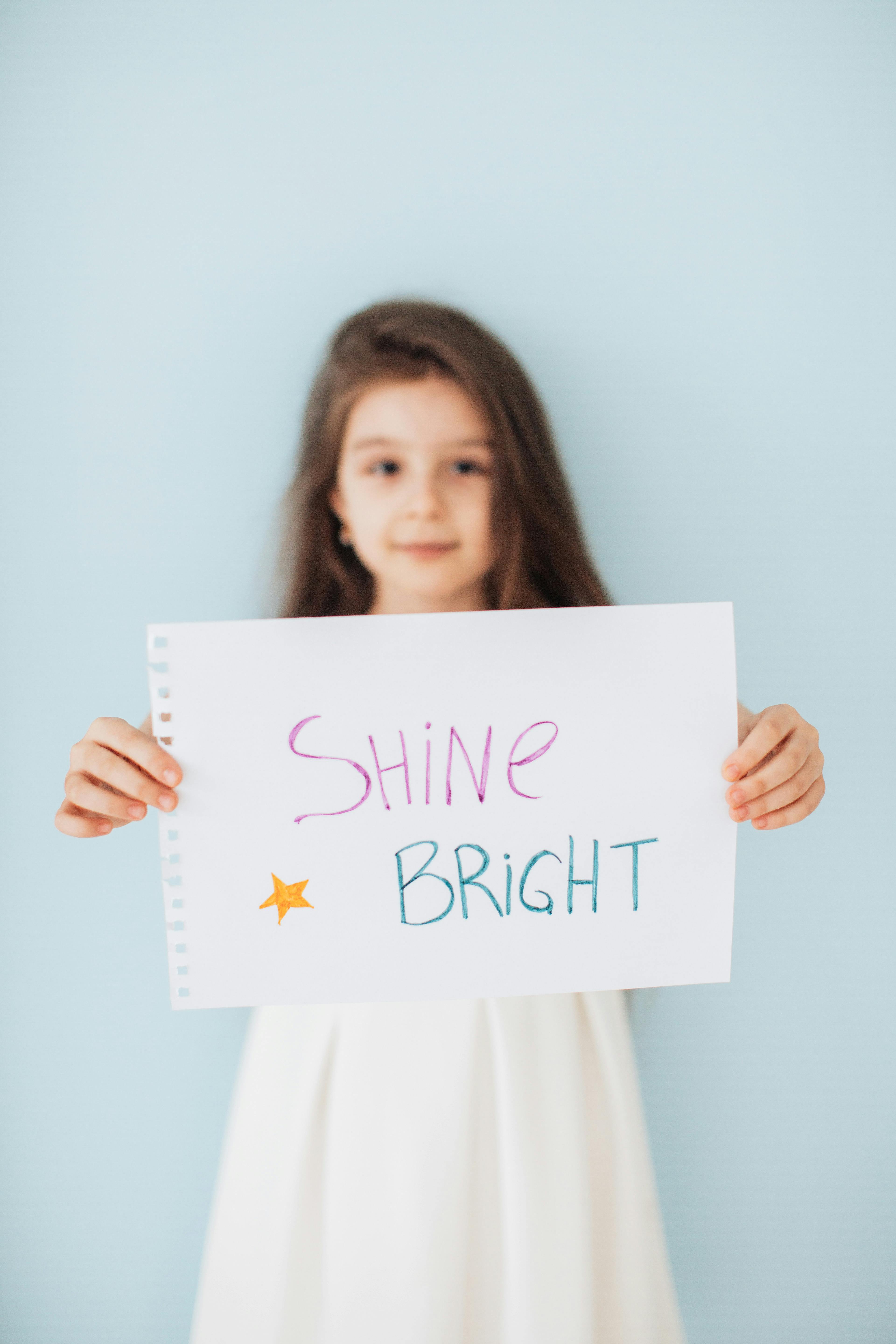 little girl holding a piece of paper with shine bright written on it