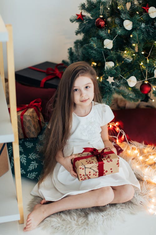 Little Girl Sitting Next to a Christmas Tree and Holding a Pres · Free ...