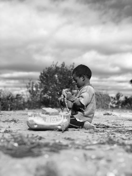 Grayscale Photo of a Boy Sitting on the Ground